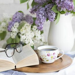 Ein kleiner Tisch mit Kaffee, Buch, Blumenstrauß und Lesebrille