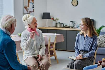 Das Bild zeigt eine Seniorin und einen Senior im Gespräch mit einer jungen Frau.