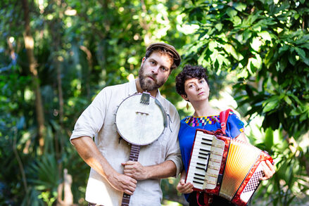 Die Künstlerin und der Künstler von Tante Friedl stehen mit ihren Instrumenten in einem botanischen Garten.