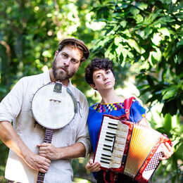 Das Duo "Tante Friedl" mit Akkordeon und Banjo vor grünen Pflanzen.